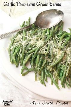 a white plate topped with green beans covered in parmesan cheese next to a spoon