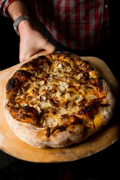 a person holding a pizza on top of a wooden cutting board