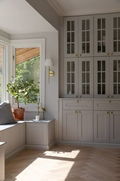 a kitchen with white cabinets and wood flooring next to a window filled with potted plants