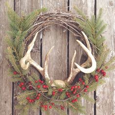 a wreath with antlers and berries is hanging on a wooden wall next to a fence