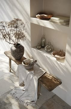 a wooden bench sitting next to a wall with shelves above it and a plant in a vase