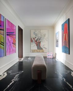 an empty room with paintings on the wall and floor in front of it, along with a bench