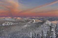 the sky is pink and orange as the sun sets in the distance over snow covered mountains