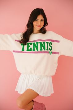 a woman is posing for the camera wearing a tennis sweater and pink boots with her arms outstretched