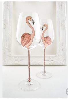 two wine glasses with pink flamingos painted on them sitting in front of a white frame