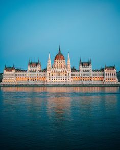 the parliament building is lit up at night with lights reflecting in the water and blue sky