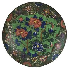 a green plate with flowers and butterflies painted on the side, in front of a white background