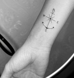 a woman's wrist tattoo with an arrow and compass on the left side of her arm