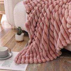 a pink blanket sitting on top of a wooden floor next to a cup and saucer