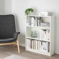 a chair sitting next to a book shelf with books on top of it and a plant in the corner