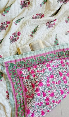 an open book laying on top of a quilted bed with pink and green flowers