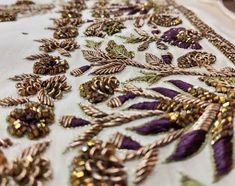 an embroidered table cloth with gold sequins and pine cones on it, along with other decorative items