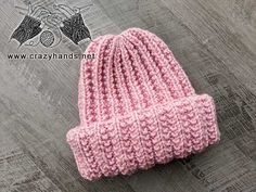 a pink knitted beanie sitting on top of a wooden floor next to a pair of scissors