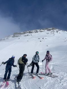 four people on skis are standing in the snow at the top of a mountain