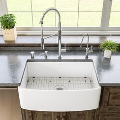 a white sink sitting under a window next to a counter top with a potted plant