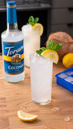 two glasses filled with ice and lemons on a table next to a bottle of tonic