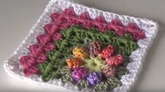 a crocheted square with flowers on the center is shown in pink, green and white