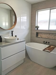 a white bath tub sitting next to a bathroom sink under a round mirror on a wall