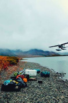 an airplane flying over a body of water with luggage on the ground next to it