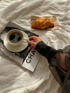 a person sitting on a bed with a cup of coffee and croissant in front of them