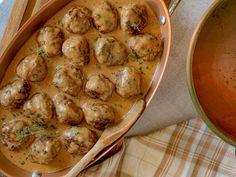 meatballs and gravy are in a dish next to a pot of sauce