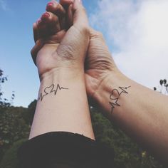 two people holding hands with small tattoos on their wrists and wrist, against a blue sky