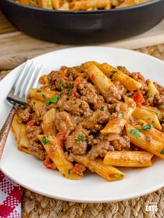 a white plate topped with pasta next to a skillet filled with meat and sauce