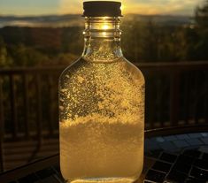 a glass bottle filled with liquid sitting on top of a table next to a window