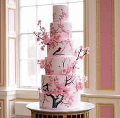 a three tiered cake with pink flowers and birds on the top is sitting on a table in front of a window