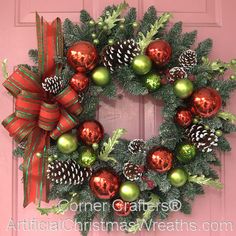 a christmas wreath with pine cones, ornaments and bows hanging on a pink front door