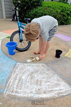 a young boy is playing with chalk on the ground next to his bike and bucket