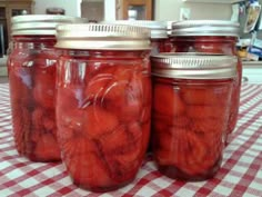 four jars filled with pickles sitting on top of a checkered tablecloth covered table