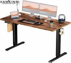 two computer monitors sitting on top of a wooden desk with black legs and a keyboard