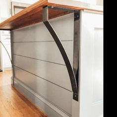 a kitchen counter with a wooden shelf and metal brackets on the top, in front of a white wall