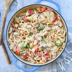 a skillet filled with pasta and vegetables on top of a blue towel next to a wooden spoon