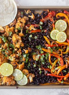 a tray filled with black beans, cauliflower, peppers and lime wedges