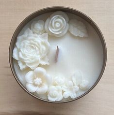 a candle with white flowers in it sitting on a table next to a wooden surface