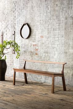 a wooden bench sitting in front of a brick wall next to a potted plant