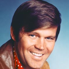 a man wearing a red and white polka dot tie smiling at the camera with his head tilted to the side