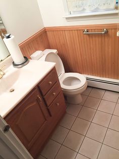 a bathroom with a toilet, sink and wooden paneling on the wall behind it