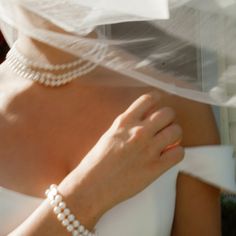 a woman in a white wedding dress with pearls on her wrist and veil over her head