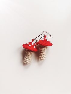 two crocheted red and white mushrooms are hanging from hooks on a white surface