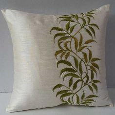 a white pillow with green leaves on the front and back, sitting on a table