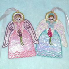 two small angel ornaments on a blue background, one with pink flowers and the other with green leaves