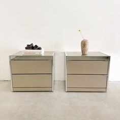 two side tables with drawers and a vase sitting on top of each one in front of a white wall