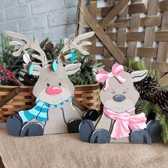 two paper reindeers sitting next to each other on top of a wooden crate filled with pine cones