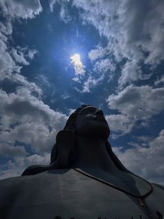 the sun is shining behind a statue with its head in the air and it's face partially obscured by clouds