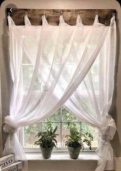 a window with white curtains and potted plants