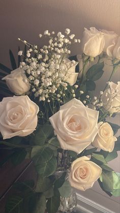 a vase filled with white roses and baby's breath in front of a mirror