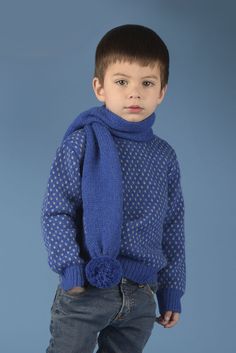 a young boy in a blue sweater and scarf poses for the camera with his hands on his hips